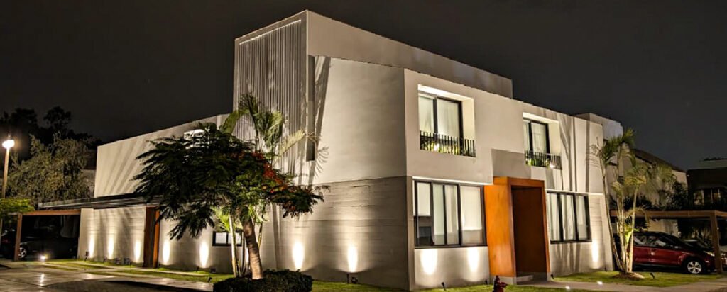 Vista exterior de Casa Siete Surco con fachada contemporánea, grandes ventanales, áreas verdes e iluminación arquitectónica.