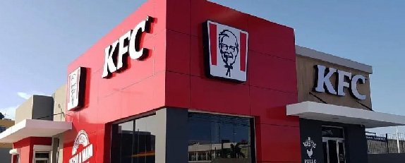 Fachada de KFC con revestimiento rojo, amplios ventanales y elementos gráficos de la marca.