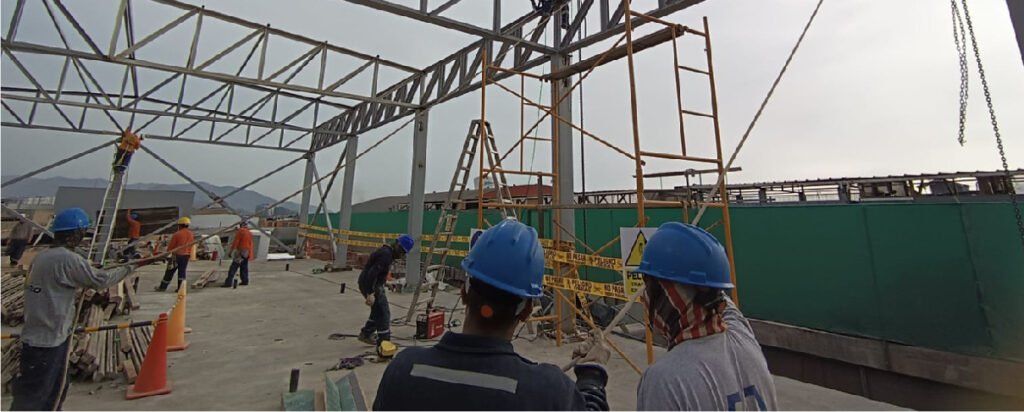 Construcción de la Planta Central Acuario con montaje de estructuras metálicas y personal trabajando en obra.