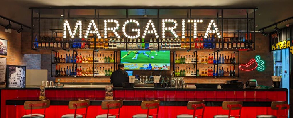 Área de bar de Chili’s con barra central, mobiliario rojo, iluminación cálida y señalética decorativa.