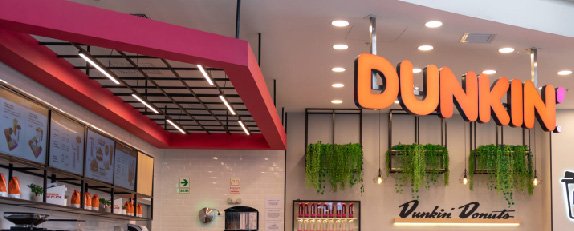 Interior de Dunkin Donuts con iluminación cálida, vegetación decorativa y elementos característicos de la marca.