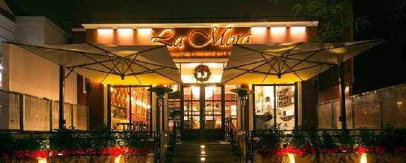 Fachada de La Mora con iluminación cálida, terraza exterior y detalles decorativos de estilo acogedor.