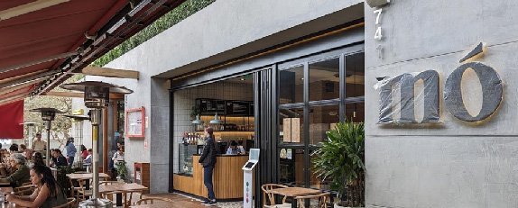 Fachada de Mó Café con terraza exterior, grandes ventanales y acabados en tonos naturales.