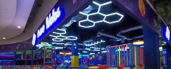 Interior de Mundo Pelotas con iluminación geométrica, áreas de juegos y elementos decorativos de colores.