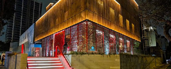 Fachada nocturna de Song con revestimiento de madera, iluminación arquitectónica y detalles decorativos en rojo.