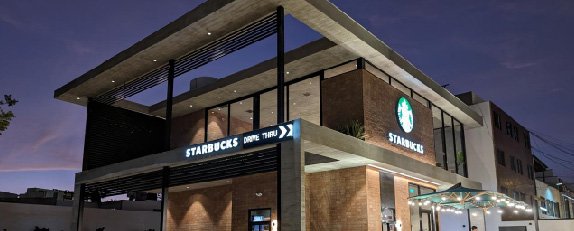 Fachada de Starbucks con estructura contemporánea, amplios ventanales y señalética iluminada.